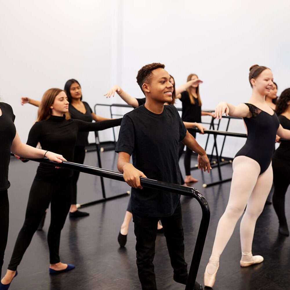 Male And Female Students At Performing Arts School Rehearsing Ballet In Dance Studio Using Barre